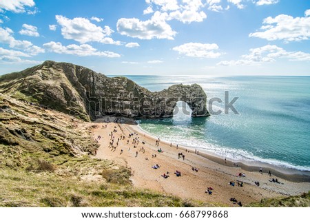 The picture of Durdle Door from the Southwest coastal path on a sunny day after a winter season with tourists on a beach.