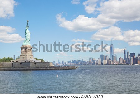 Statue of Liberty island and New York city skyline in a sunny day, white clouds