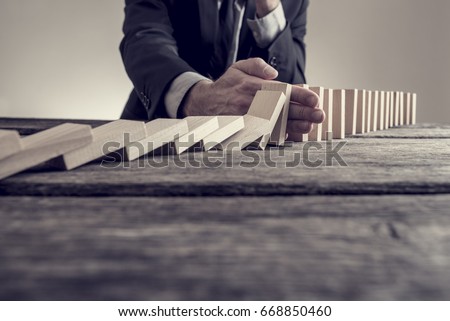 Retro effect faded and toned image of a businessman stopping domino effect on wooden table. Business solution concept. Royalty-Free Stock Photo #668850460