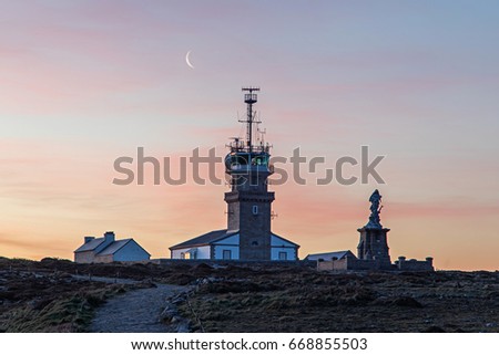Beautiful view of famous Phare of Pointe du Raz on Cape Sizun at sunset in summer with the moon on background, Brittany, northern France - colored filter