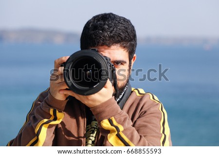 Young cheerful photographer with beard, while working outside making seascape pictures and looking on camera