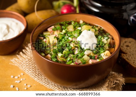 Okroshka. Traditional Russian summer cold soup with sausage, vegetables and kvass in bowl on wooden background. Selective focus.