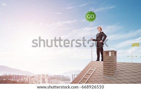 Young caucasian businessman standing on house roof and holding go green sign. Mixed media