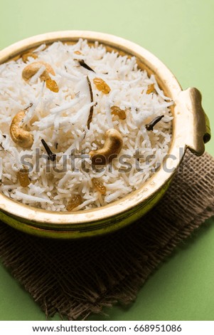 Sweet Coconut Rice OR Narali Bhat in Marathi, garnished with Cashew, Cloves & Dry fruits, served in a brass bowl over moody background. Selective focus