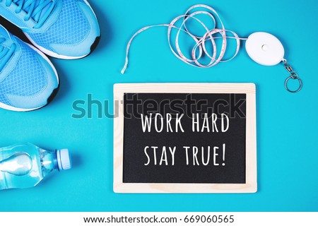 Fitness background made of sneakers, bottled water, measuring tape and chalkboard with text WORK HARD STAY TRUE as motivation. Blue background. Concept of healthy lifestyle. Flat lay style of picture