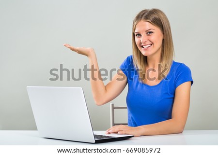 Beautiful young woman is showing palm of hand  while using computer.Young girl with laptop gesturing