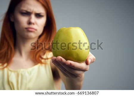 Emotions, diet, healthy diet, fruit, young woman on a gray background holding an apple.