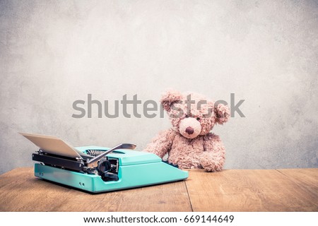 Teddy Bear toy sitting at the old wooden desk with mint green retro typewriter front concrete wall background. Vintage style filtered photo