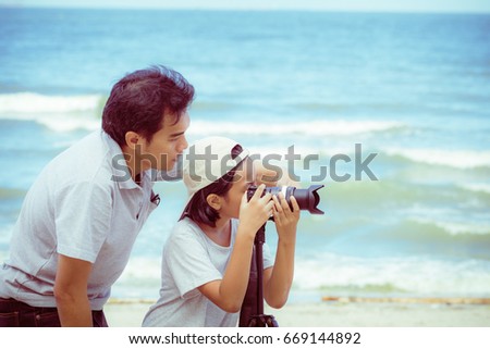 Dad is teaching her daughter to take pictures on the beach on a summer holiday with vintage color tone
