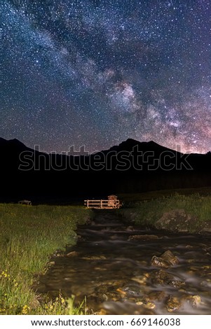  Milky Way rising over a wooden bridge in the italian alps - The real colors of milky way galaxy, astronomic picture. A slight noise is normal for this type of photos. Noisy image.