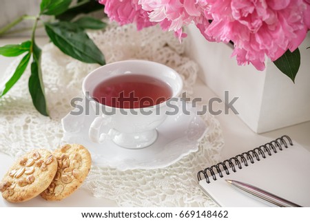 Red berry or fruit tea in white porcelain teacup on a white table with peony bouquet, cookies and notebook. Writing day plans, romantic note, Mothers day concept