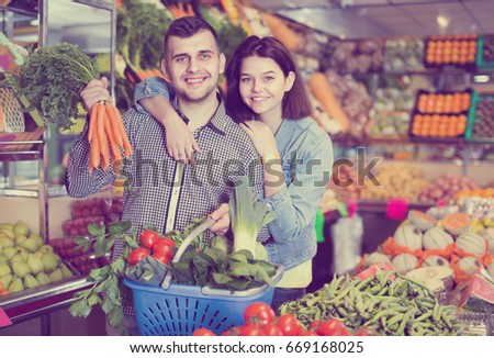 Loving couple are deciding on vegetables in grocery shop. 