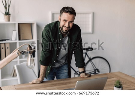 smiling bearded businessman leaning on table in modern office