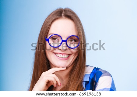 Studying, education and fun concept. Happy smiling nerdy woman in weird big glasses. Studio shot on blue background