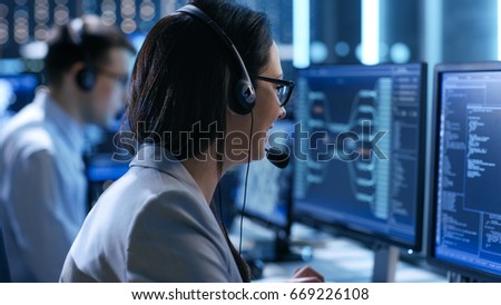 In the System Control Center Woman working in a Technical Support Team Gives Instructions with the Help of the Headsets. Possible Air Traffic/ Power Plant/ Security Room Theme. Royalty-Free Stock Photo #669226108
