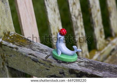 A child's plastic toy of a performing seal and a ball left behind on the arm of a park bench