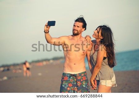 Couple walking on beach at sunset taking selfie picture on mobile phone relaxing together