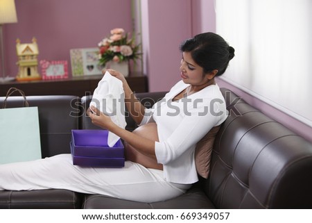 Pregnant mother opening gifts of baby clothes 