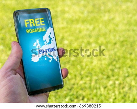 Free Roaming in Europe. Smart phone in hand concept. Green summer grass background.