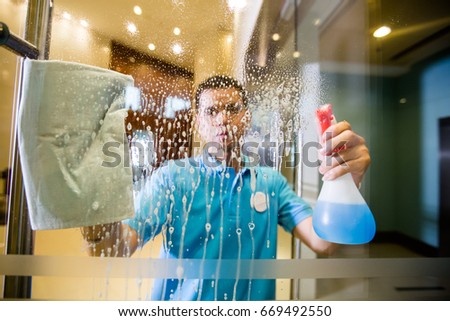 Man is cleaning window with spray, Picture can be illustration to article of sanitary. Royalty-Free Stock Photo #669492550