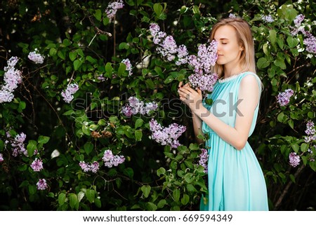 Blonde girl with bouquet of wild flowers outdoors A model in a turquoise dress against a background of a lilac bush.