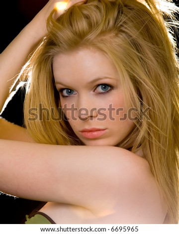 Attractive close up of face of a woman with long blond hair and blue eyes with serious expression over black