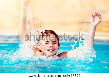 Happy cheerful child having fun in the pool, jumping and splashing water, with pleasure spending time in the refreshing water, summer time activity, carefree and happy childhood