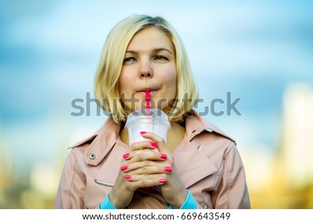 Portrait of blonde drinking milkshake in park, blurred background