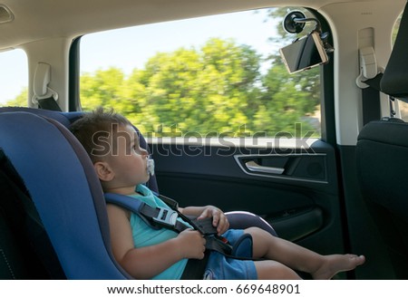 Baby boy in a car on child safety seat watching cartoon on the tablet