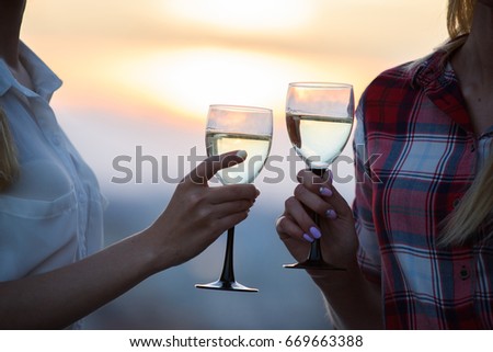 Two female friends clinking wine glasses close to the sea during the sunset. Summer lifestyle concept. Glasses of wine in the hands of women.