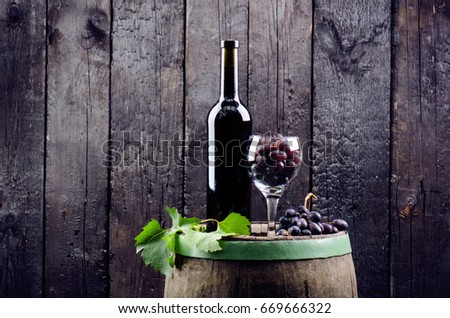 Glass and bottle of wine on a wooden barrel. Burnt, black wooden background.  Vintage. Copyspace for a text. Grapes and green vine.
