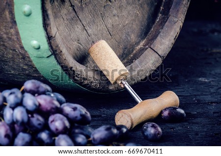 Corkscrew next to a wooden wine barrel. Wine on a wooden barrel. Burnt, black wooden background. Vintage. Copyspace for a text. Grapes and green vine. 