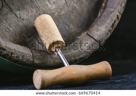 Corkscrew next to a wooden wine barrel. Wine on a wooden barrel. Burnt, black wooden background. Vintage. Copyspace for a text. Grapes and green vine. 