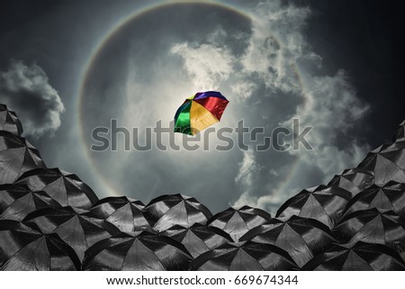 Conceptual image with colorful umbrella among many black ones