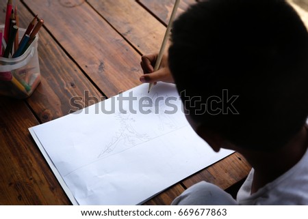 A boy is drawing cartoon with pencil in white paper on wooden table.