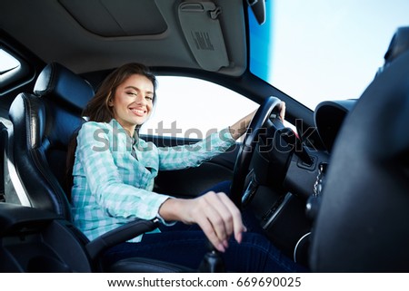 Beautiful girl wearing blue shirt sitting in automobile looking at camera and smiling