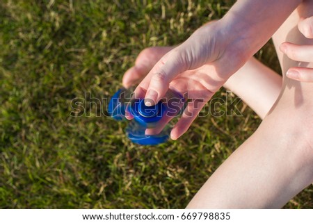 Girl with a Tri Fidget Hand Spinner on her hand outdoors. Green grass in the background.