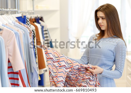 Attractive young woman looking disappointed and unhappy choosing dresses at the clothing store poor quality not impressed shopping fashion negativity sales retail consumerism customer client service Royalty-Free Stock Photo #669810493