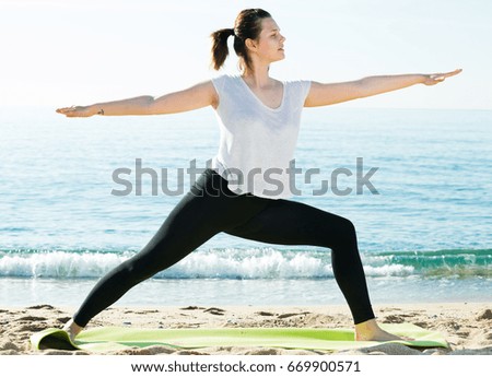 Woman in white T-shirt is stretching on the beach.