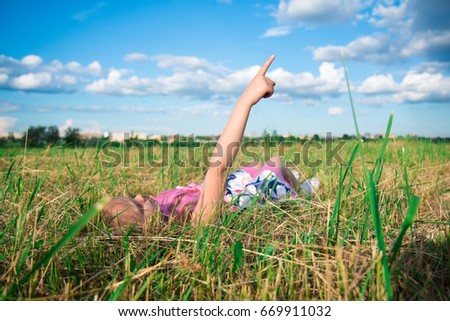 Happy dreamy girl lies in the park on grass and shows on clouds, dreams