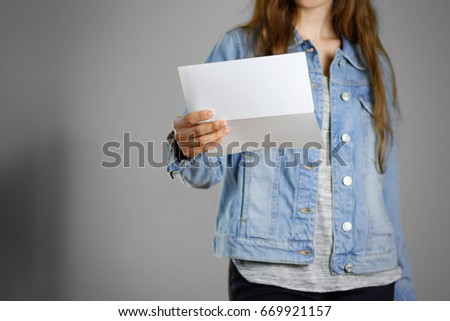 The girl in the blue denim shirt holds the white empty piece of paper. Ready for your design. Closeup. Isolated