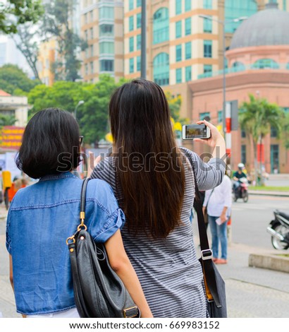 Back view of womans taking pictures by mobile phone in the city