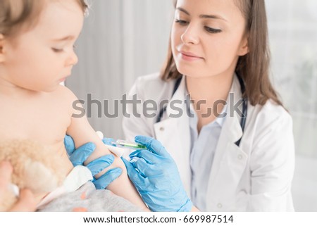 Young woman pediatrician performs a vaccination of a little girl. The girl is holding a mascot.