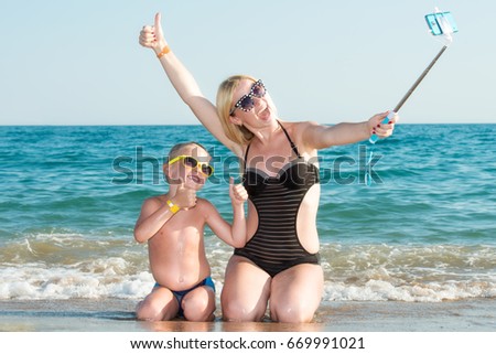 Mother and son in bathing suits and sunglasses taking a selfie on a mobile phone on the sea coast.