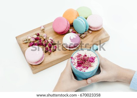 View woman hands holding a blue cappuccino cup with roses petals and beauty french macarons. White background table