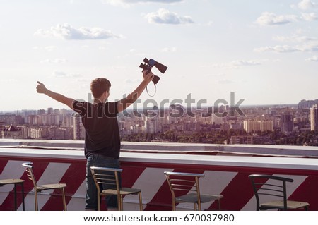 A young man observes through binoculars on the roof of a tall building