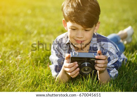 Cute young boy lying on green grass at the park holding vintage camera taking pictures of nature copyspace outdoors people lifestyle children hobby leisure childhood photography photographer summer