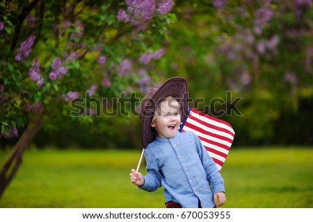 Cute toddler boy holding american flag in beautiful park. Independence Day concept.