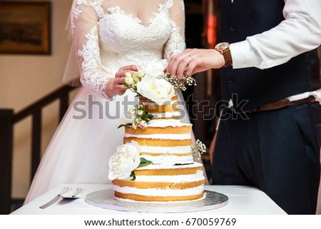 Bride and groom at wedding reception cutting the wedding cake with flowers. Royalty-Free Stock Photo #670059769