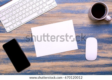Office workplace with keyboard, empty paper, mobile phone, cup of tea and computer mouse on a wooden background. Flat lay, top view. Blue peeling paint. Flat lay design, View from above.